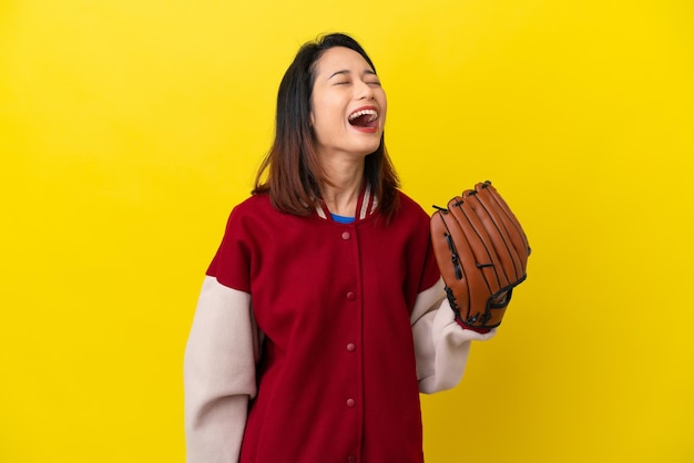 Young Vietnamese player woman with baseball glove isolated on yellow background laughing