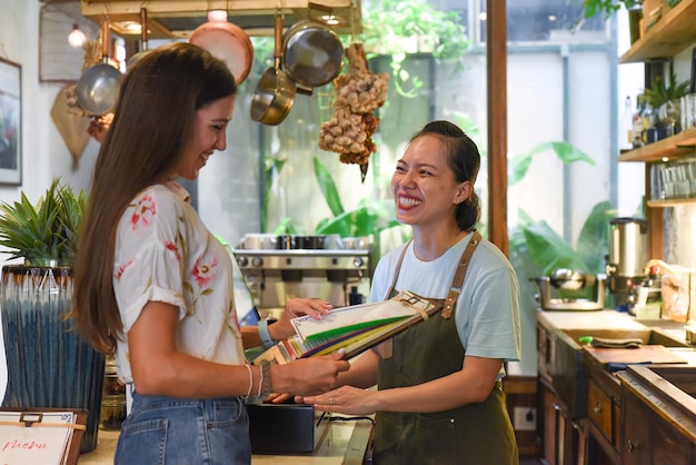 Young Vietnamese waitress working with check out machine and customers in cafe