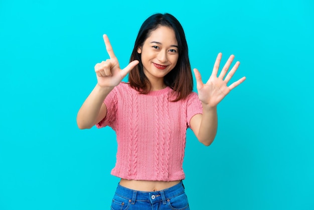 파란색 배경에 고립되어 손가락으로 7을 세는 젊은 베트남 여성