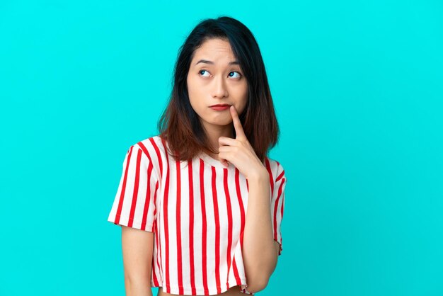 Young Vietnamese woman isolated on blue background having doubts and thinking