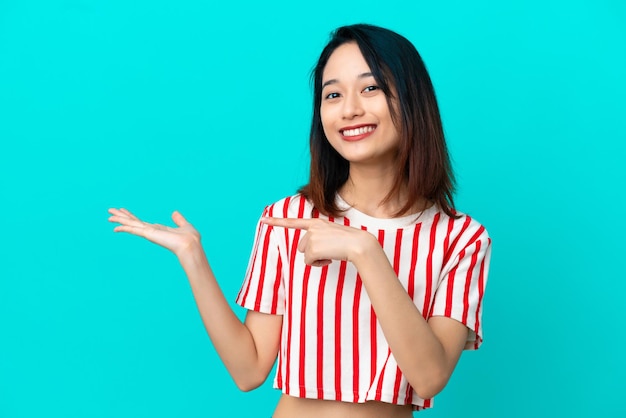 Young Vietnamese woman isolated on blue background holding copyspace imaginary on the palm to insert an ad