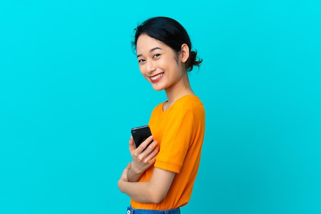 Young Vietnamese woman isolated on blue background holding a mobile phone and with arms crossed