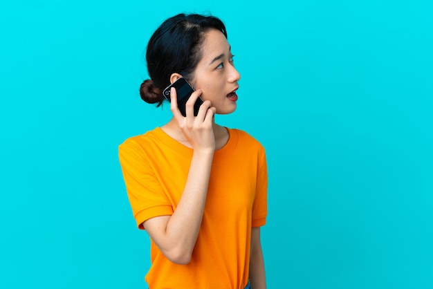 誰かと携帯電話で会話をしながら青い背景に孤立した若いベトナム人女性