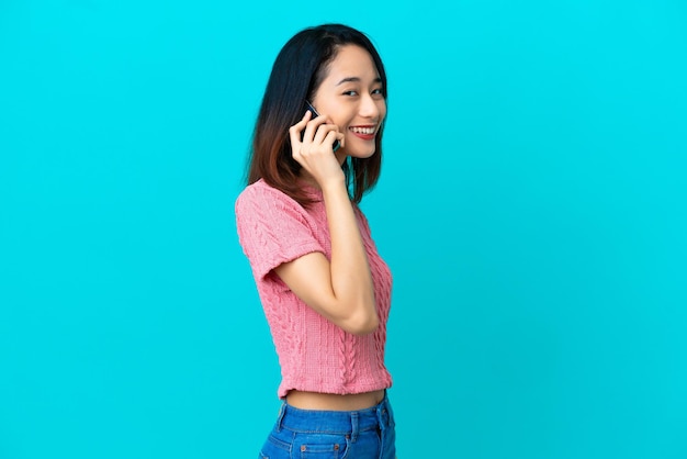 Young Vietnamese woman isolated on blue background keeping a conversation with the mobile phone with someone