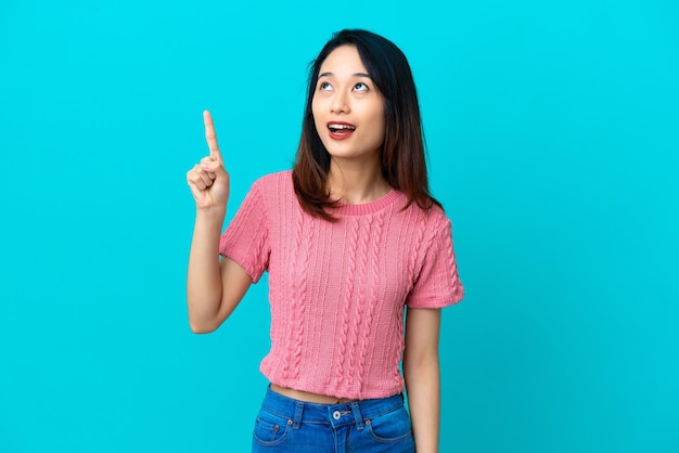 Young Vietnamese woman isolated on blue background pointing up and surprised