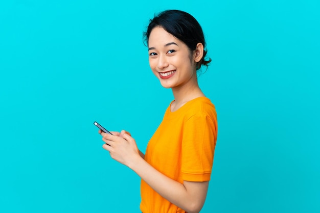 Young Vietnamese woman isolated on blue background sending a message or email with the mobile