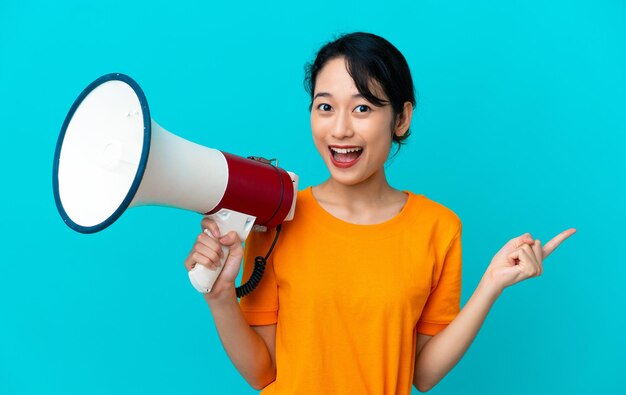 Young Vietnamese woman isolated on blue background shouting through a megaphone and pointing side