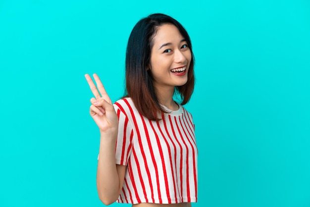 Молодая вьетнамская женщина на синем фоне улыбается и показывает знак победы