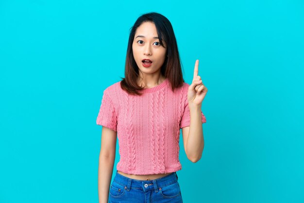 Young Vietnamese woman isolated on blue background thinking an idea pointing the finger up