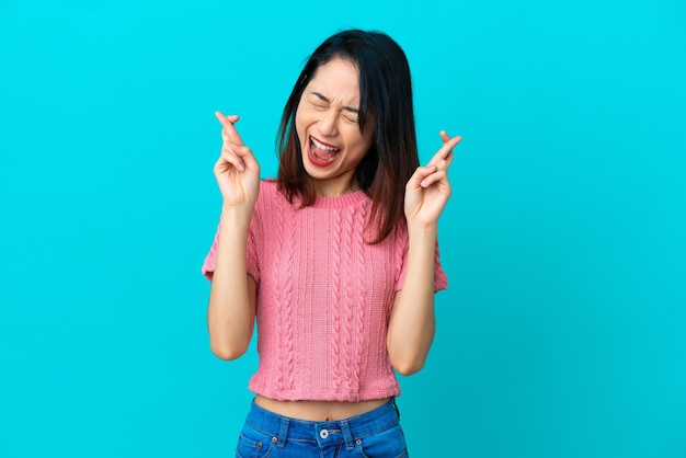 Young Vietnamese woman isolated on blue background with fingers crossing