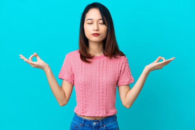 Young Vietnamese woman isolated on blue background in zen pose