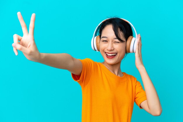 音楽を聴いて歌う青い背景に分離された若いベトナム人女性