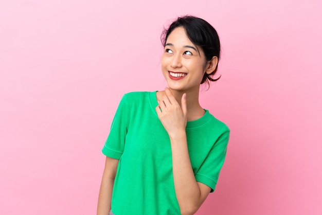 Young Vietnamese woman isolated on pink background looking up while smiling