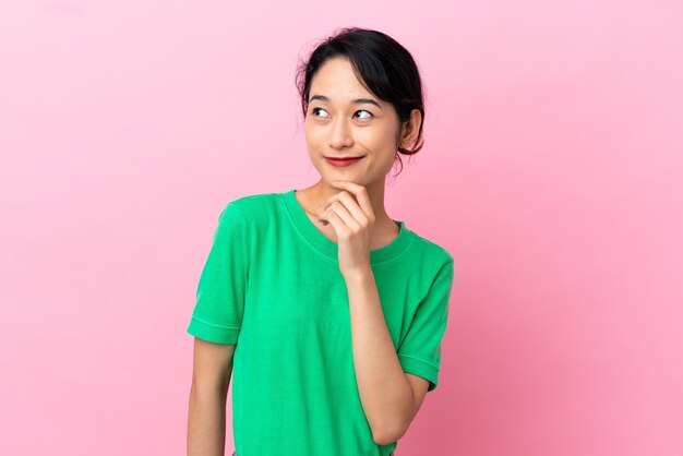 Young Vietnamese woman isolated on pink background and looking up