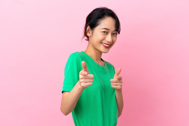 Young Vietnamese woman isolated on pink background pointing to the front and smiling