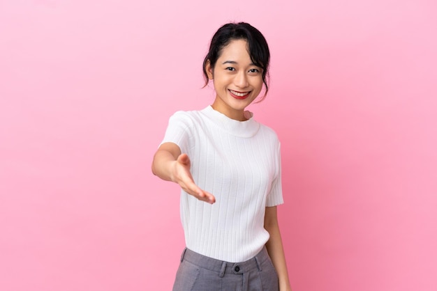 Young Vietnamese woman isolated on pink background shaking hands for closing a good deal