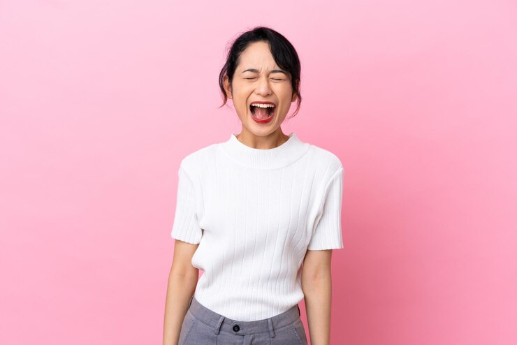 Photo 口を大きく開いて正面に叫んでピンクの背景に孤立した若いベトナム人女性
