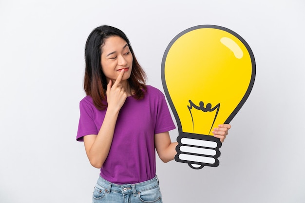 Young Vietnamese woman isolated on white background holding a bulb icon and having doubts