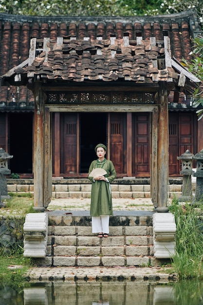 Foto giovane donna vietnamita nel tradizionale abito ao dai in piedi sui gradini di fronte al vecchio biulding