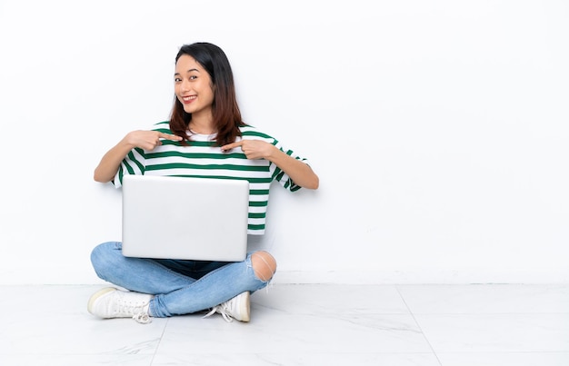 Young Vietnamese woman with a laptop sitting on the floor isolated on white wall proud and self-satisfied