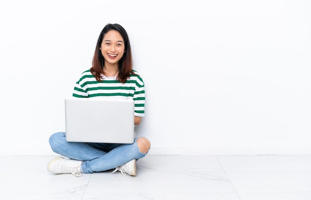 Young Vietnamese woman with a laptop sitting on the floor isolated on white wall with surprise facial expression