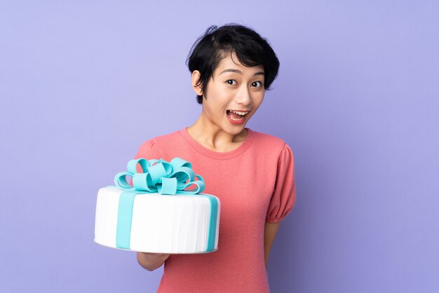 Young Vietnamese woman with short hair holding a big cake over purple wall