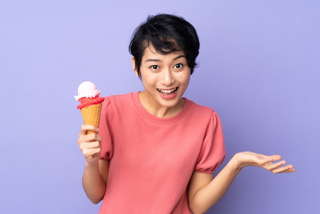 Young Vietnamese woman with short hair holding a cornet ice cream over purple wall with shocked facial expression