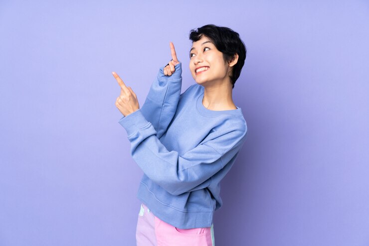 Photo 人差し指で素晴らしい分離を指している孤立した紫の上の短い髪の若いベトナム人女性