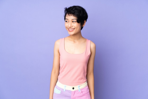 Young Vietnamese woman with short hair over purple wall looking side