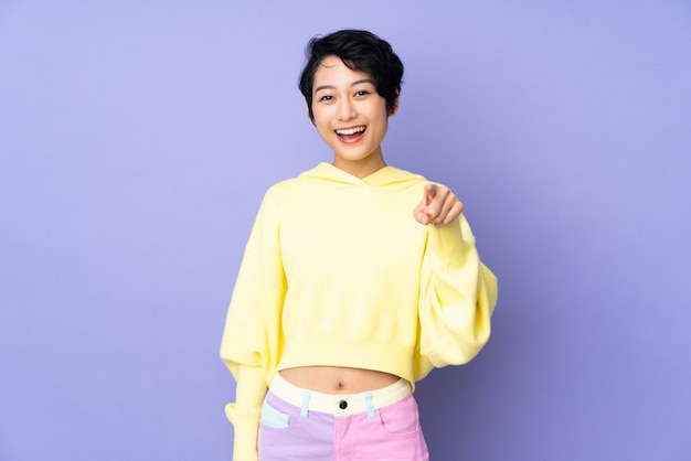 Young Vietnamese woman with short hair over purple wall surprised and pointing front