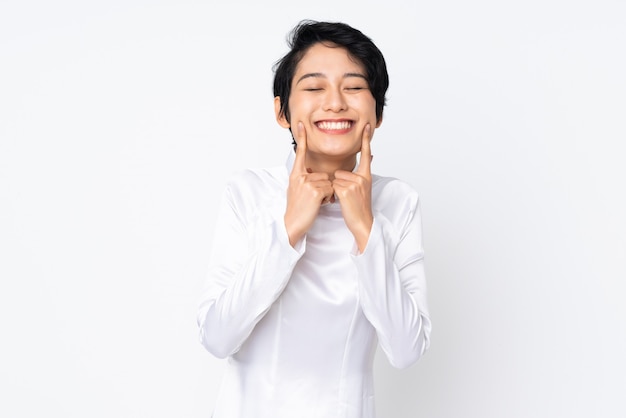 Young Vietnamese woman with short hair wearing a traditional dress over white wall smiling with a happy and pleased expression