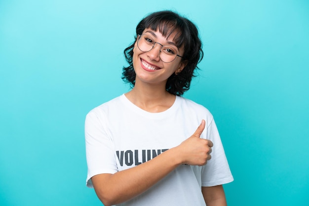 Young volunteer Argentinian woman isolated on blue background giving a thumbs up gesture