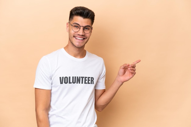 Young volunteer caucasian man isolated on beige background pointing finger to the side