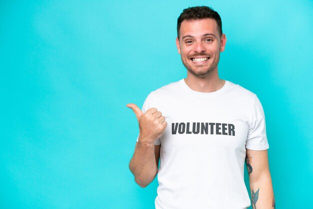 Young volunteer caucasian man isolated on blue background pointing to the side to present a product