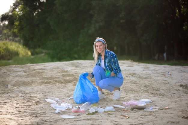 Giovane volontario raccogliendo bottiglie di plastica sulla spiaggia vicino al parco.