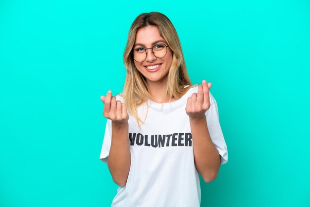 Young volunteer Uruguayan woman isolated on blue background making money gesture