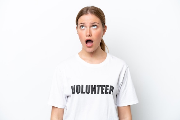 Молодая женщина-волонтер, изолированная на белом фоне, смотрит вверх и с удивленным выражением лица