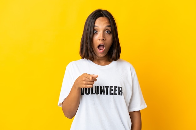 Young volunteer woman isolated on yellow surprised and pointing front