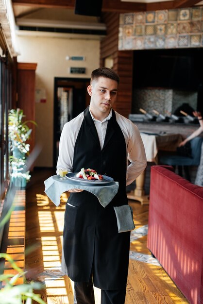 Foto un giovane cameriere con un'elegante uniforme porta una squisita insalata a un cliente in un bellissimo ristorante gourmet servizio al tavolo nel ristorante