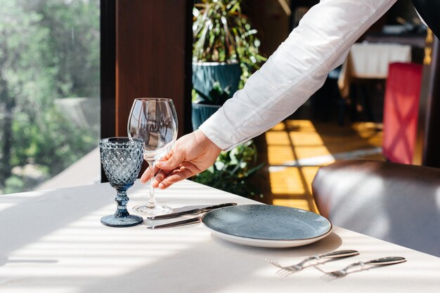 A young waiter in a stylish uniform is engaged in serving the\
table in a beautiful gourmet restaurant close-up. restaurant\
activity, of the highest level.