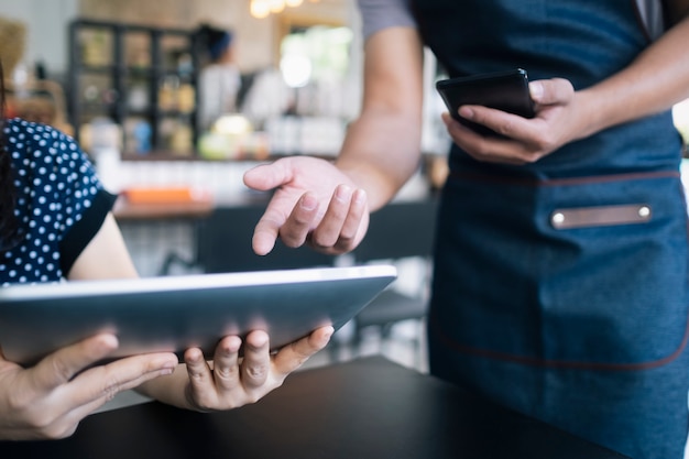 Foto giovane cameriere che utilizza una tavoletta digitale per mostrare il menu a un cliente.