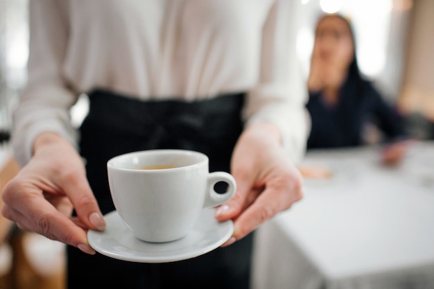 手で一杯のコーヒーを保持している若いウェイトレス