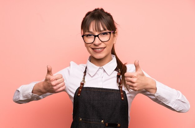 Young waitress over pink  giving a thumbs up gesture