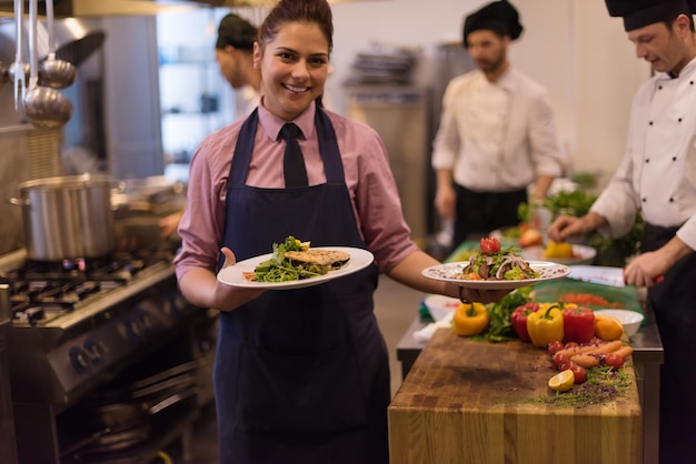 young waitress presenting dishes of tasty meals in commercial kitchen