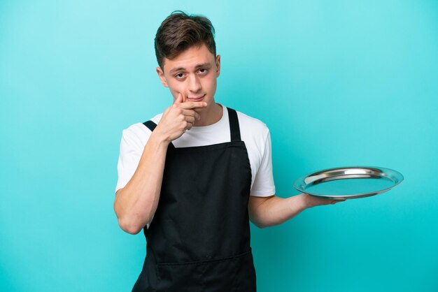 Young waitress with tray isolated on blue background thinking