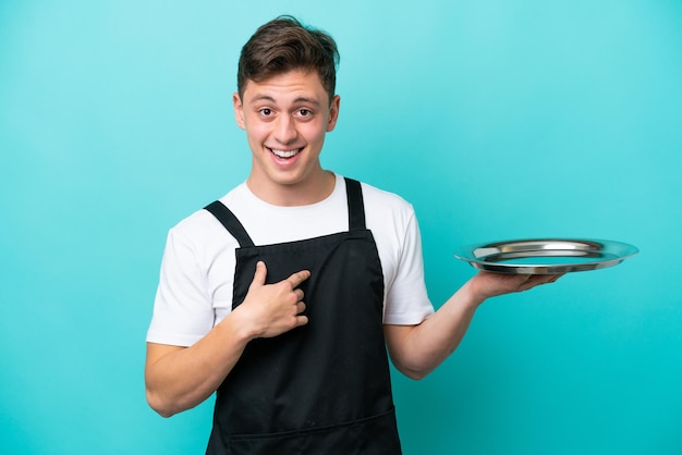 Young waitress with tray isolated on blue background with surprise facial expression