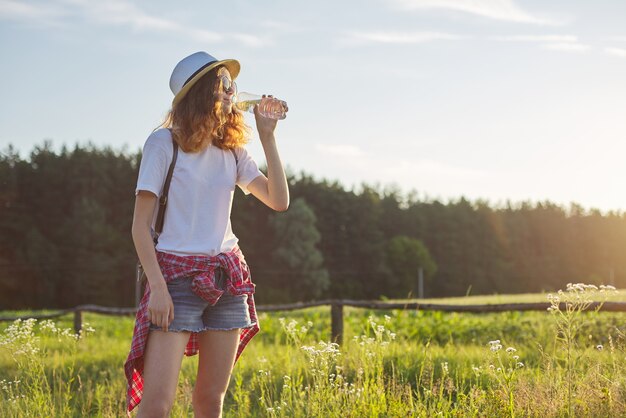 Photo young walking teen girl drinking water from a bottle. background nature