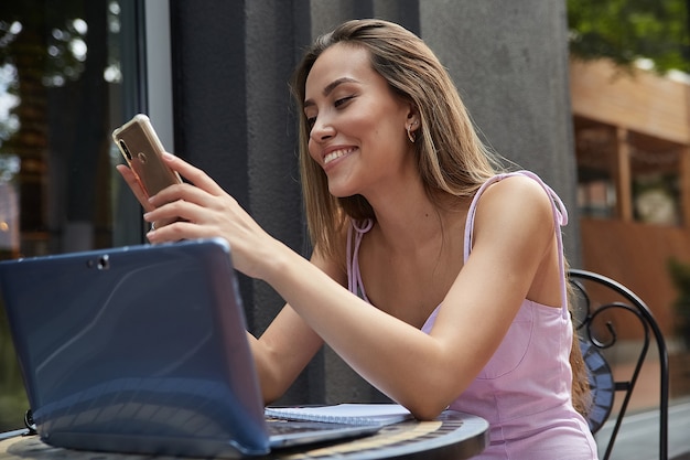 Молодая хорошо одетая азиатская женщина, сидящая за столом, используя свой смартфон. леди за пределами кафе серфинга в Интернете по мобильному телефону, болтает в Интернете. современные коммуникационные технологии, удаленная работа, удаленная работа