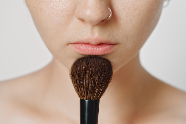 Una giovane bella ragazza bianca con una spazzola per il trucco si mette il trucco sul viso. cipria per il viso.