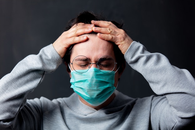 Giovane uomo bianco in occhiali e maschera protettiva con mal di testa